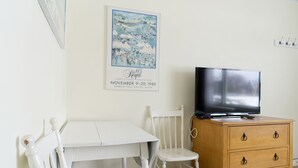 A room with a white table, a white chair, a wooden dresser with a television on top, and a poster on the wall. - Lakeside Inn (Ramara)