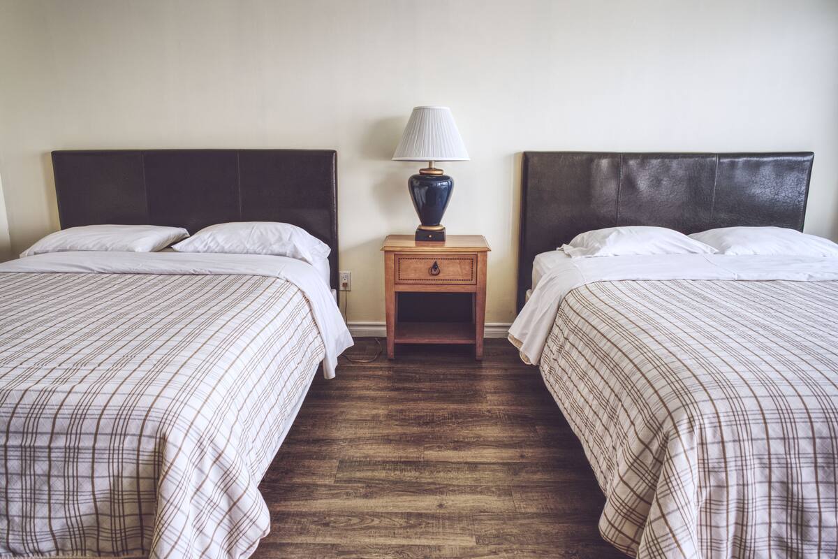 A hotel room with two beds, a nightstand with a lamp, and a wooden floor.