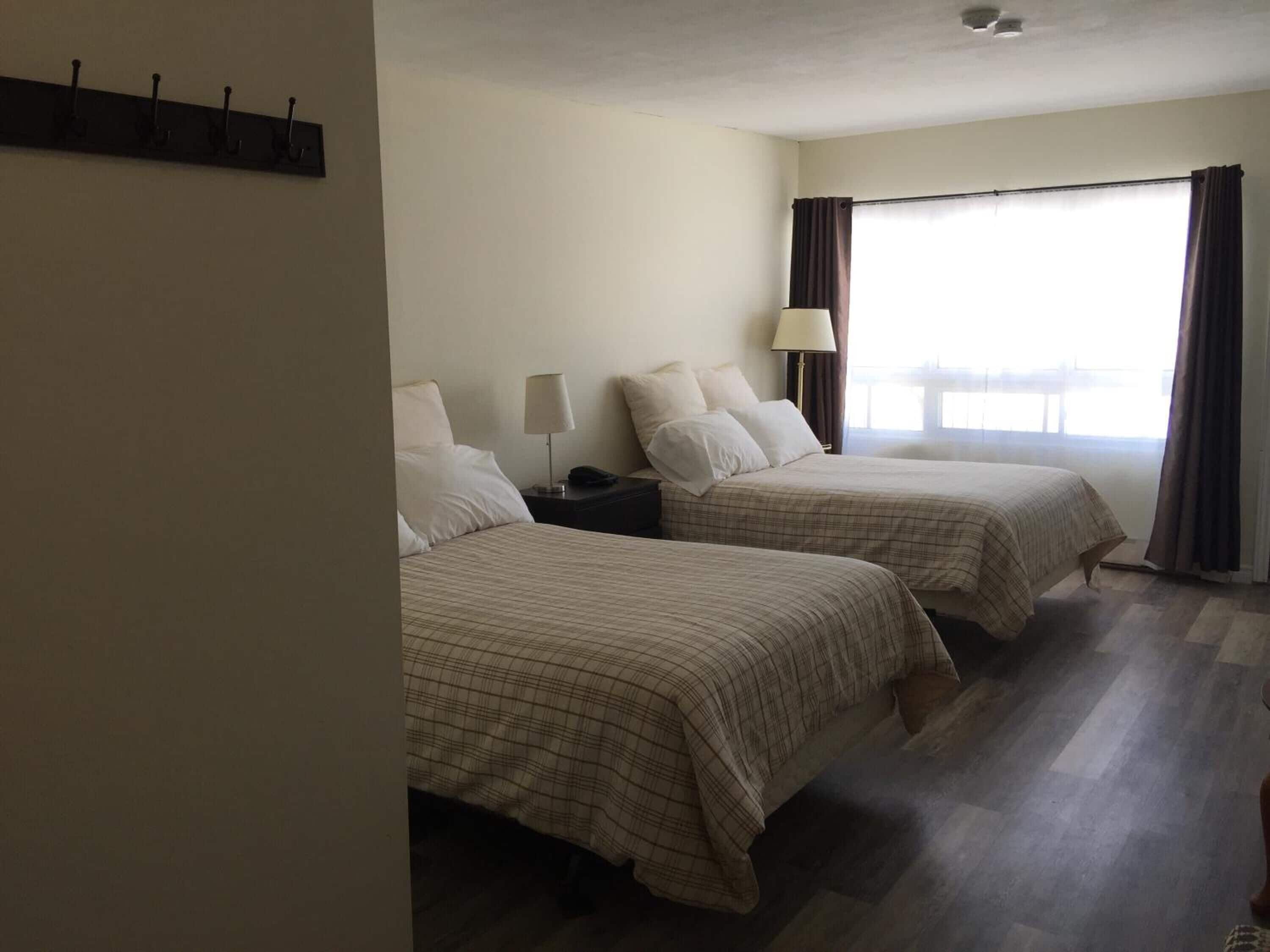 Una habitación de hotel con dos camas, una mesita de noche, una lámpara y una ventana con cortinas.