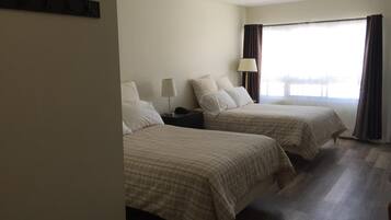 Una habitación de hotel con dos camas, una mesita de noche, una lámpara y una ventana con cortinas.