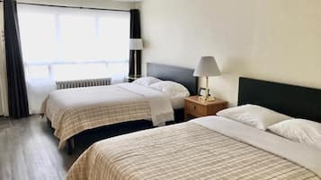 Habitación de hotel con dos camas, una ventana con cortinas, un radiador y una mesita de noche con lámpara.