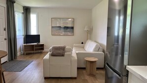 A modern living room with a sofa, a small round table, a flat-screen TV, and a refrigerator. - Lakeside Inn (Ramara)