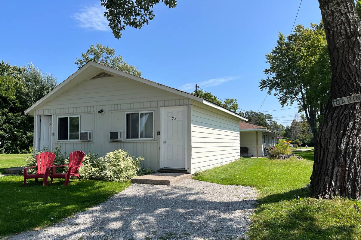 A single-story cabin with a gravel driveway, a covered porch, and a small front yard.