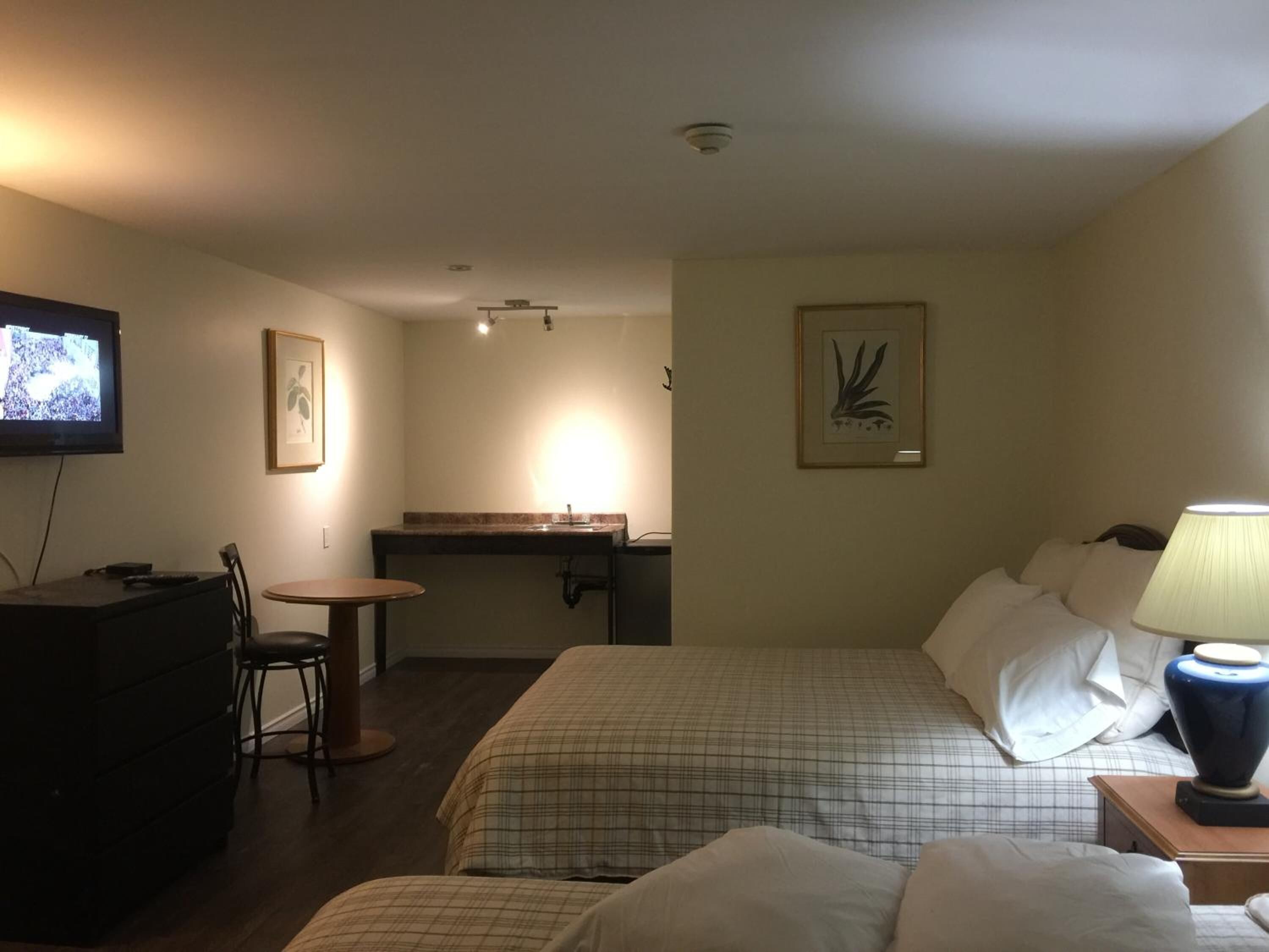 A hotel room with two beds, a desk, a chair, a television, and a lamp.