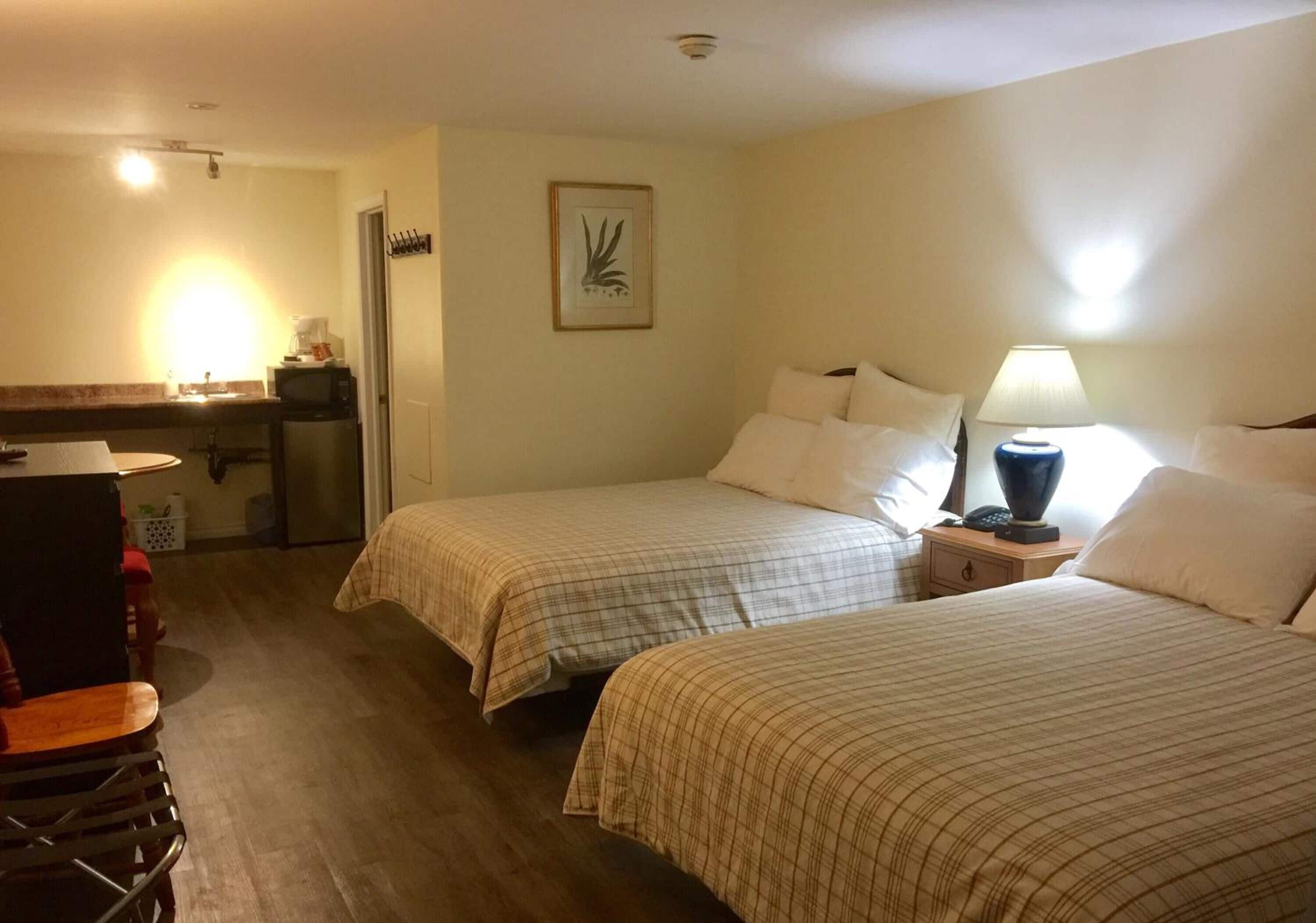 Une chambre d’hôtel avec deux lits, un bureau avec une chaise, un four à micro-ondes et une petite table avec une lampe.