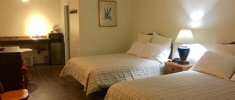 Une chambre d’hôtel avec deux lits, un bureau avec une chaise, un four à micro-ondes et une petite table avec une lampe.