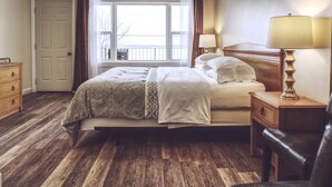A bedroom with a bed, wooden nightstands, a dresser, and a window with curtains. - Lakeside Inn (Ramara)