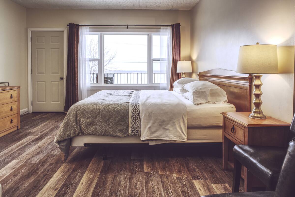 A bedroom with a bed, wooden nightstands, a dresser, and a window with curtains.