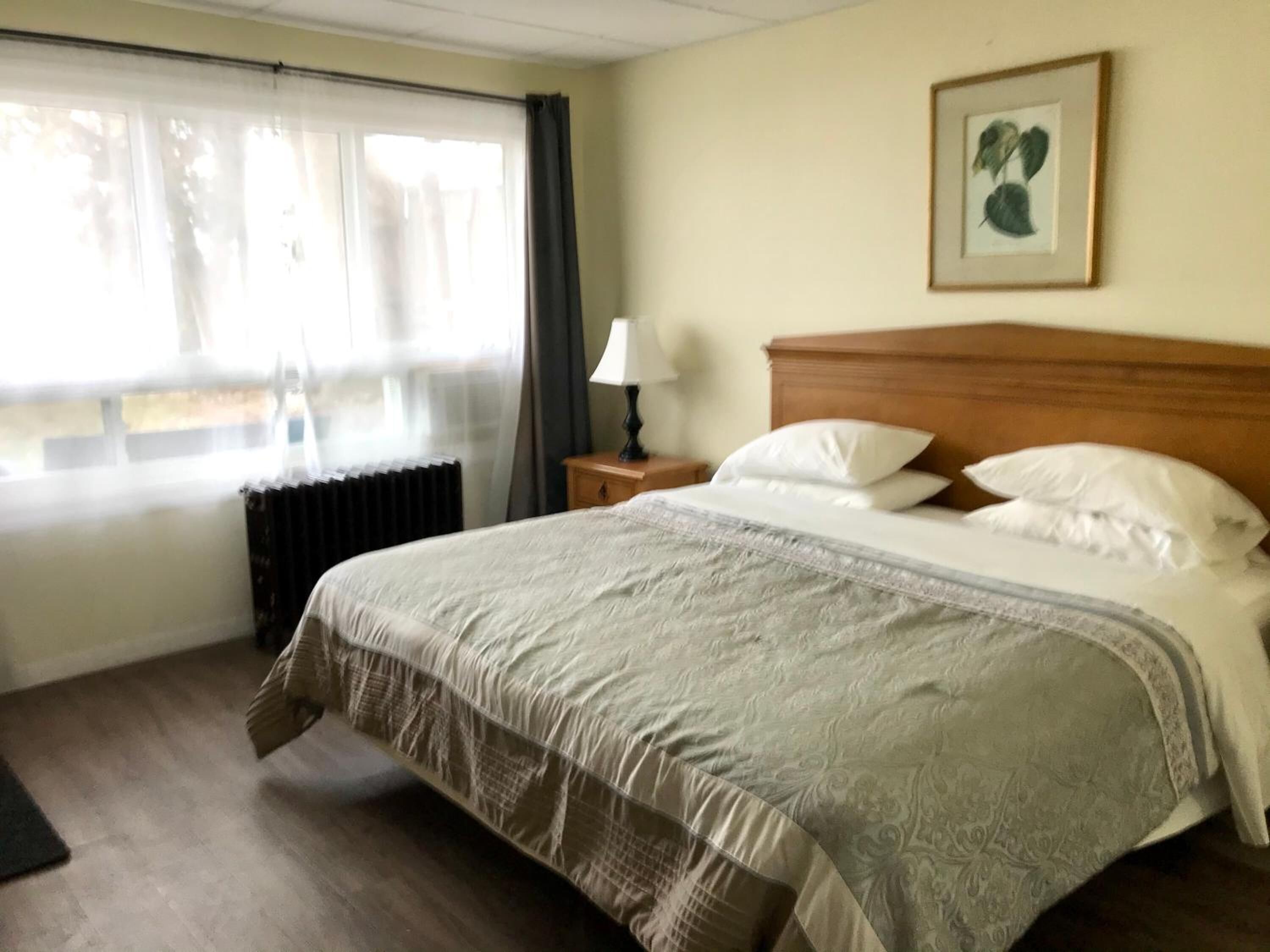 Et hotelværelse med en stor seng, et natbord med lampe, en radiator og et vindue med gardiner.