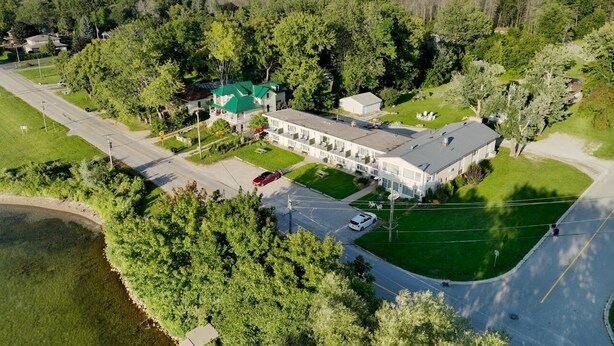 A large, single-story building with a green roof, surrounded by lush greenery and a small parking area. - Lakeside Inn (Ramara)