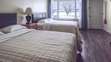 A hotel room with two beds, a nightstand, a lamp, a window with a view of trees, and a door.