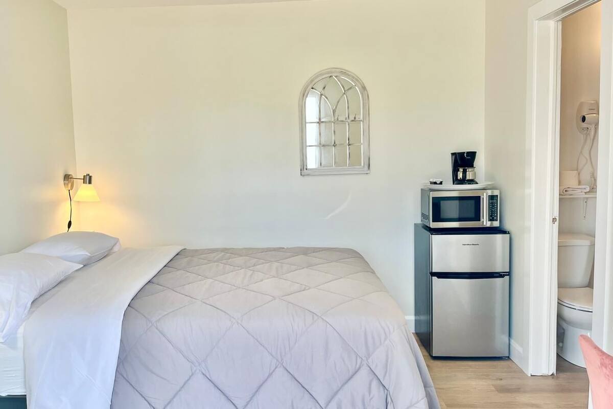 A bedroom with a bed, a bedside lamp, a microwave, and a refrigerator.