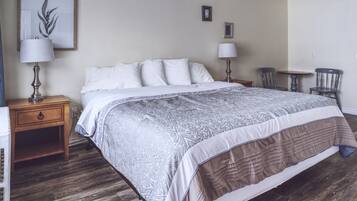 A neatly arranged bedroom with a large bed, two bedside tables with lamps, a small table with chairs, and a framed picture on the wall.