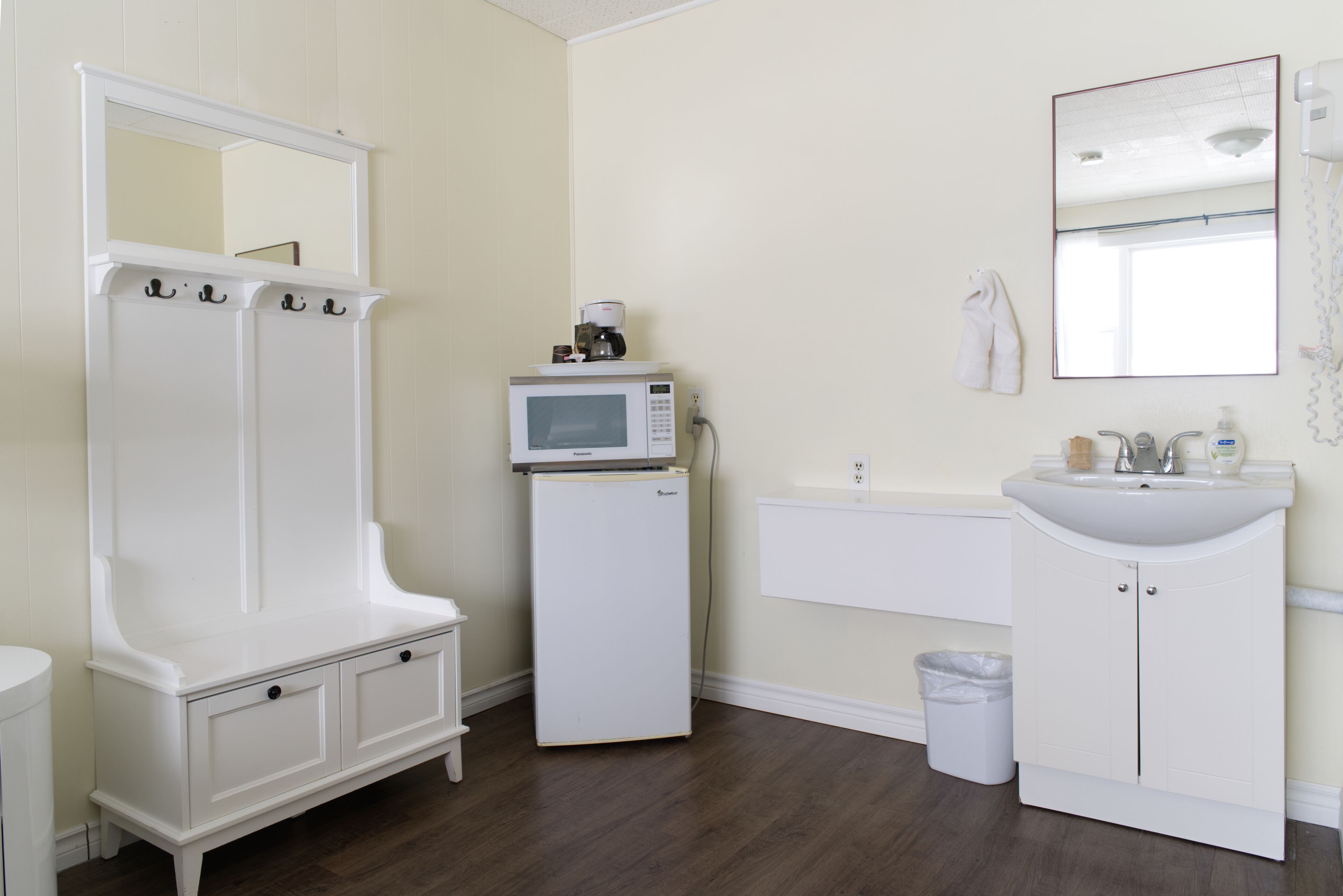 A bathroom with a white vanity, a sink, a mirror, a microwave, and a trash can.