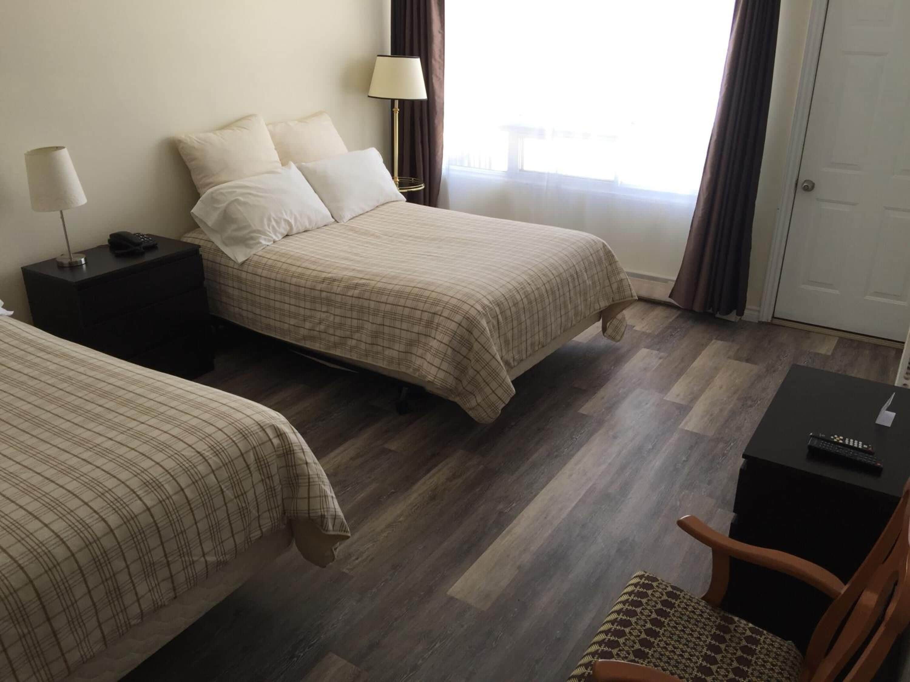 A hotel room with two beds, a desk, a chair, and a lamp.