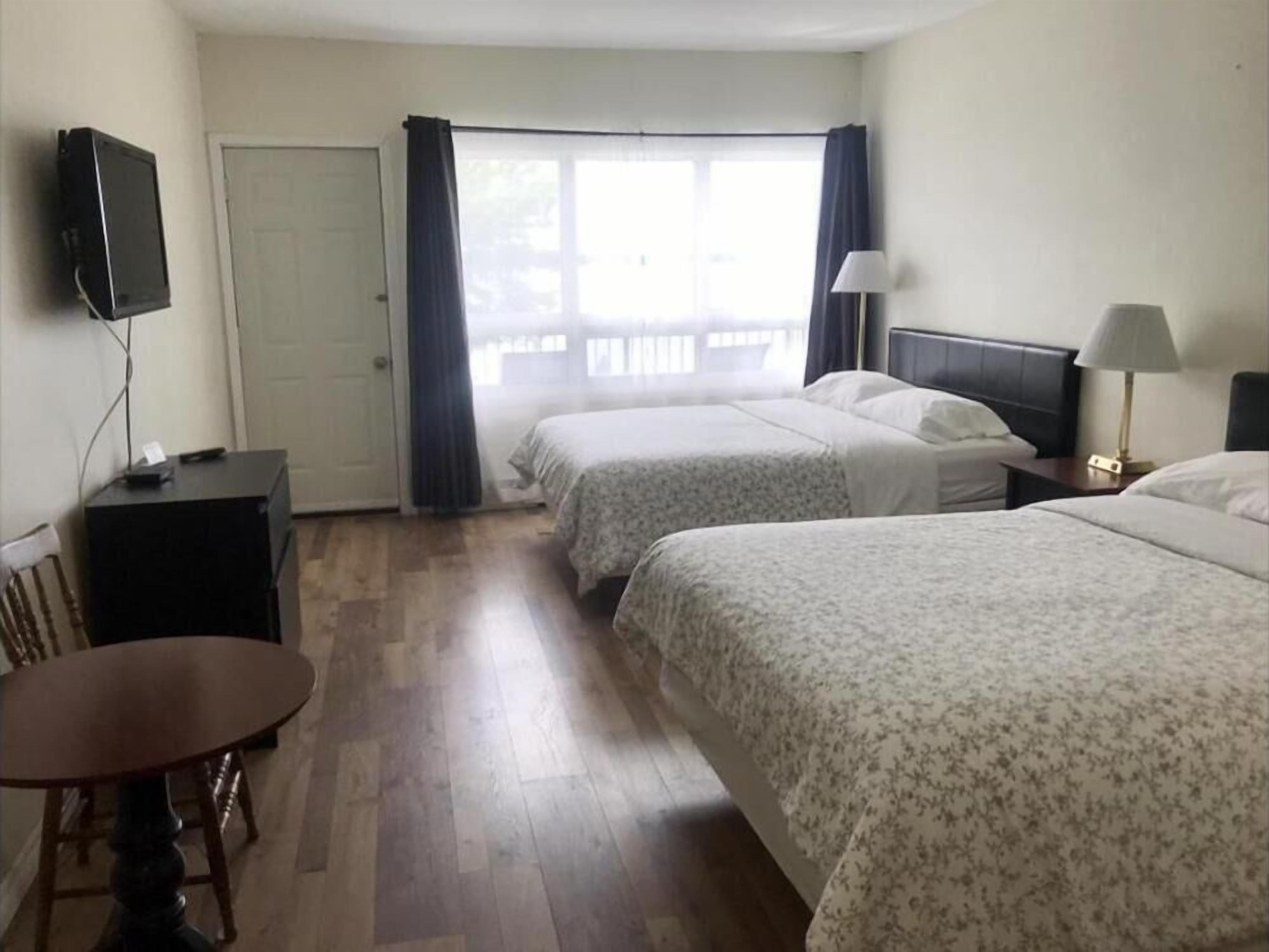 Habitación de hotel con dos camas, un escritorio, una silla, un televisor y una ventana con cortinas.