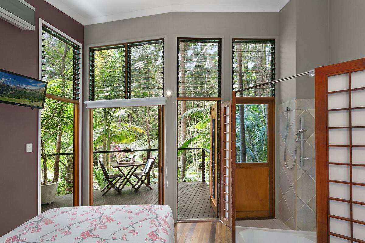 A bedroom with a large bed, a shower, and a balcony with a table and chairs.