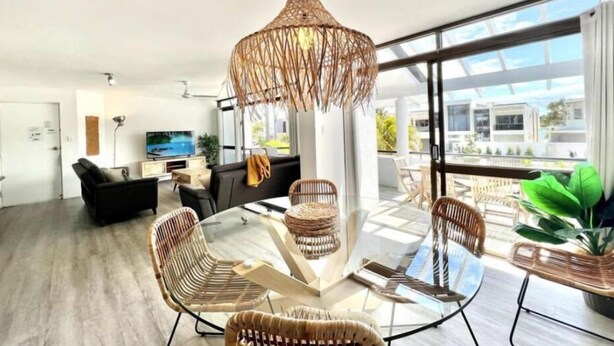 Ein modernes Wohnzimmer mit einem Glastisch, Korbstühlen, einem schwarzen Sofa und einem großen Fenster mit Blick auf die Stadt.