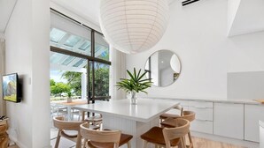 Eine moderne Küche mit einer weißen Kücheninsel, Barhocker, einem Blumentopf und einem großen Fenster.