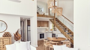 Ein modernes Interieur mit einer Holztreppe, einem Essbereich mit rundem Tisch und einer Küche mit weißen Schränken.