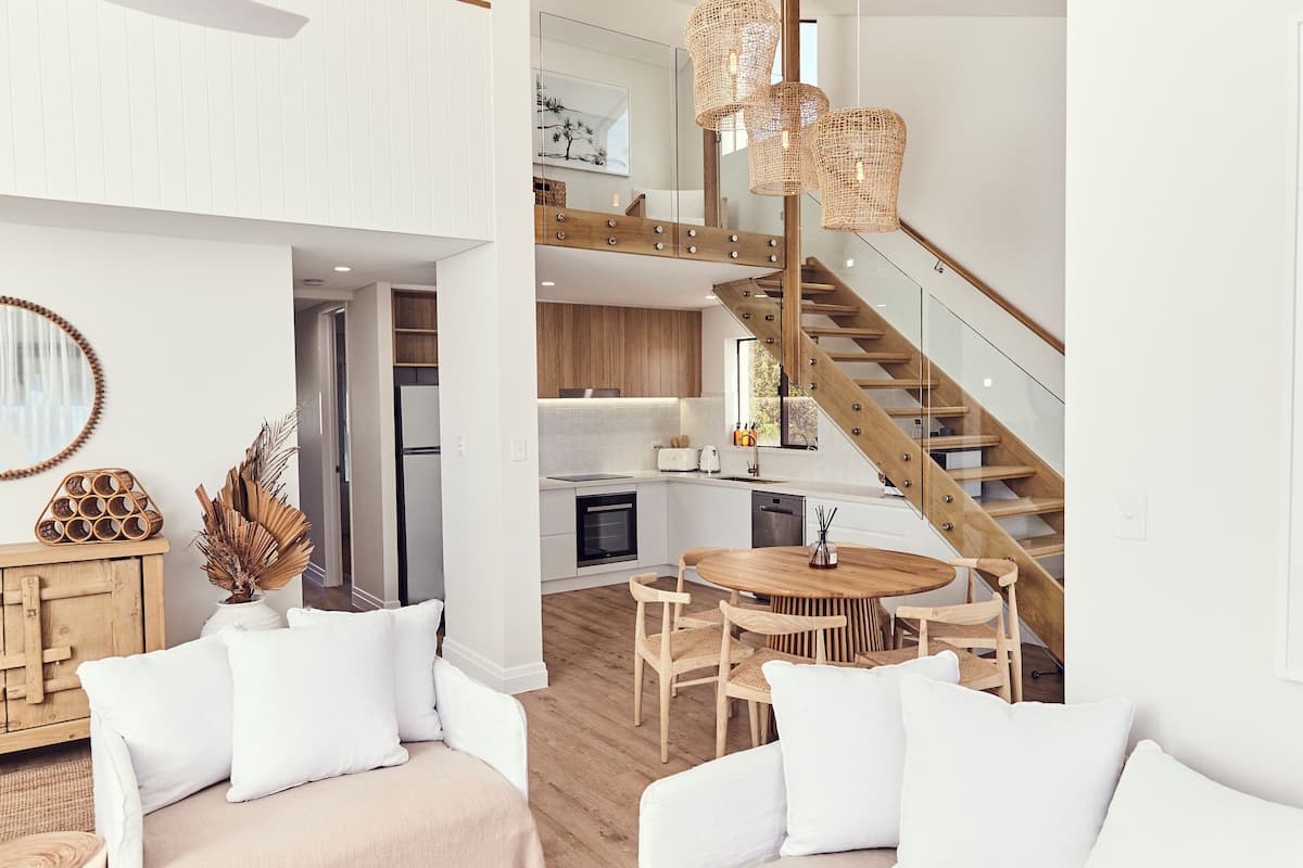 Un intérieur moderne avec un escalier en bois, un coin repas doté d’une table ronde et une cuisine aux meubles blancs.