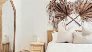 Ein Schlafzimmer mit einem hölzernen Kopfteil, einem großen Spiegel, einem Nachttisch mit Korb und einer wandmontierten Pflanzenanordnung.