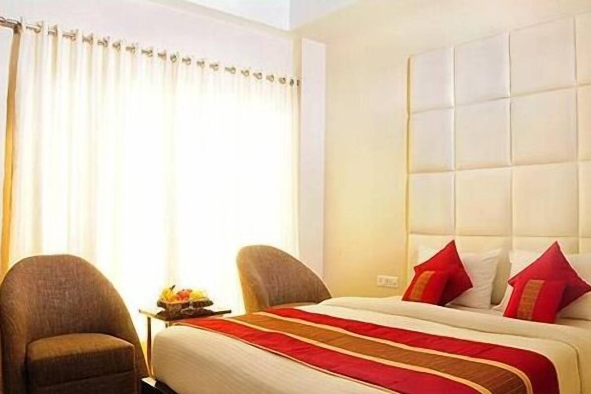 A hotel room with a large bed, two armchairs, a bedside table, and a window with curtains.