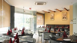 A restaurant with glass partitions, tables with red napkins, and framed pictures on the walls. - Hotel Gulnar (New Delhi)