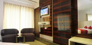 Une chambre d’hôtel avec un grand lit, un téléviseur fixé au mur, un coin salon avec deux fauteuils et une armoire avec un miroir.