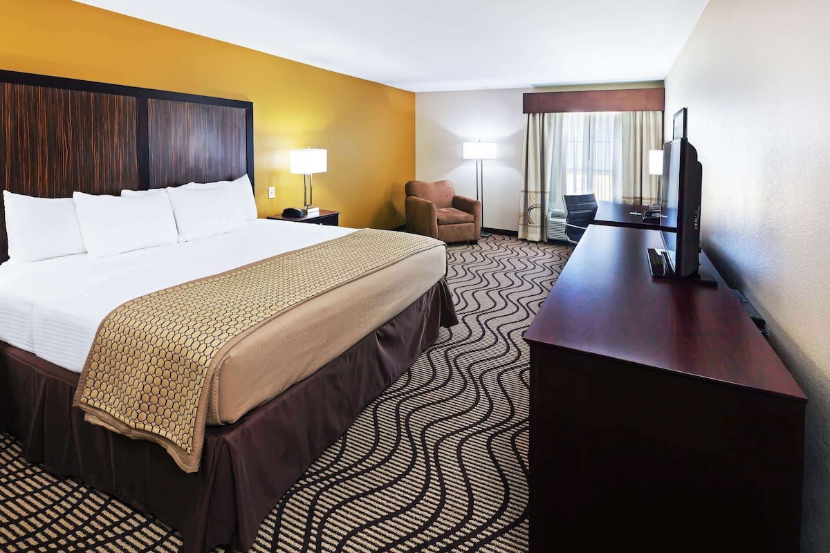 A hotel room with a large bed, a desk, a chair, a television, and a window with curtains.