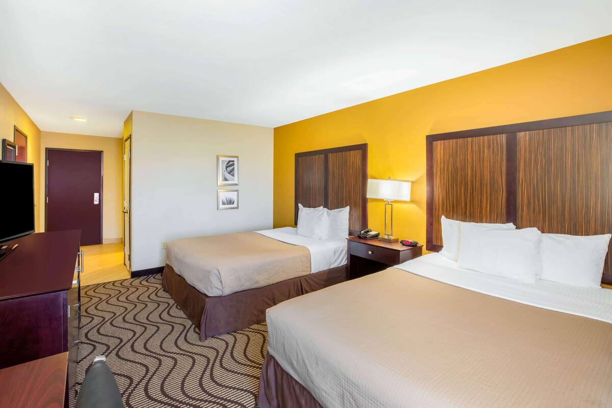 A hotel room with two beds, a desk, a TV, and a lamp.