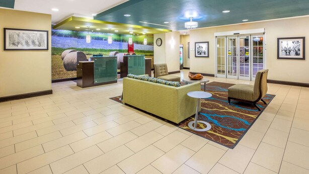 A lobby with a reception desk, a sofa, a chair, and a patterned rug. - La Quinta Inn & Suites by Wyndham Floresville (Floresville)