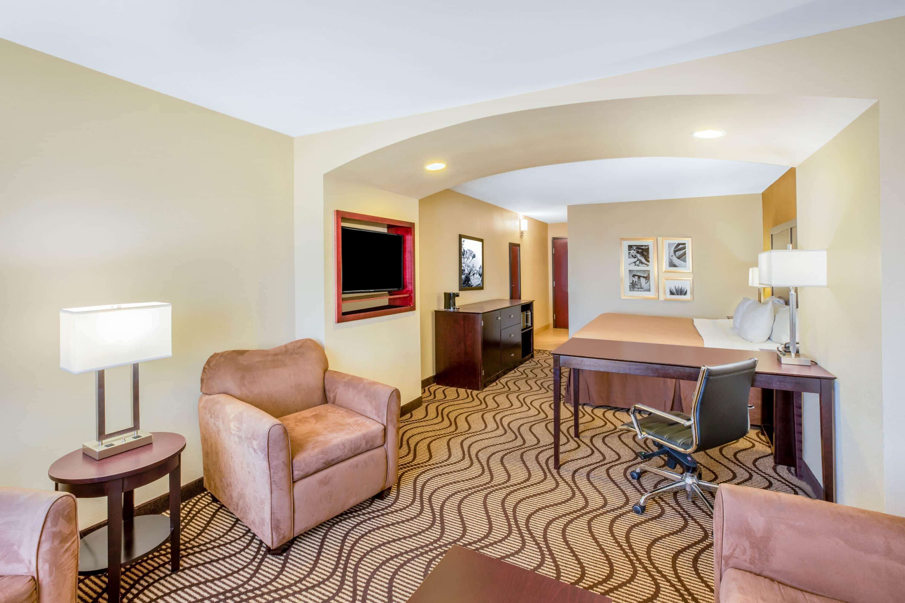 A hotel room with a bed, two armchairs, a desk, a TV, and a desk lamp.