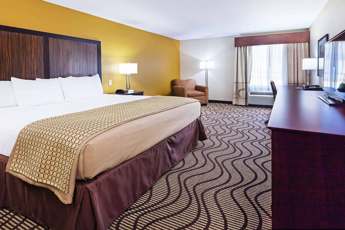 A hotel room with a large bed, a desk, a chair, and a window with curtains.