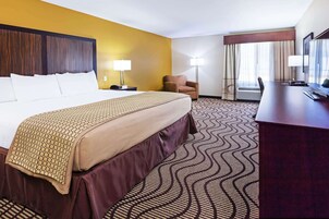 Una habitación de hotel con una cama grande, un escritorio, una silla y un ventanal con cortinas.