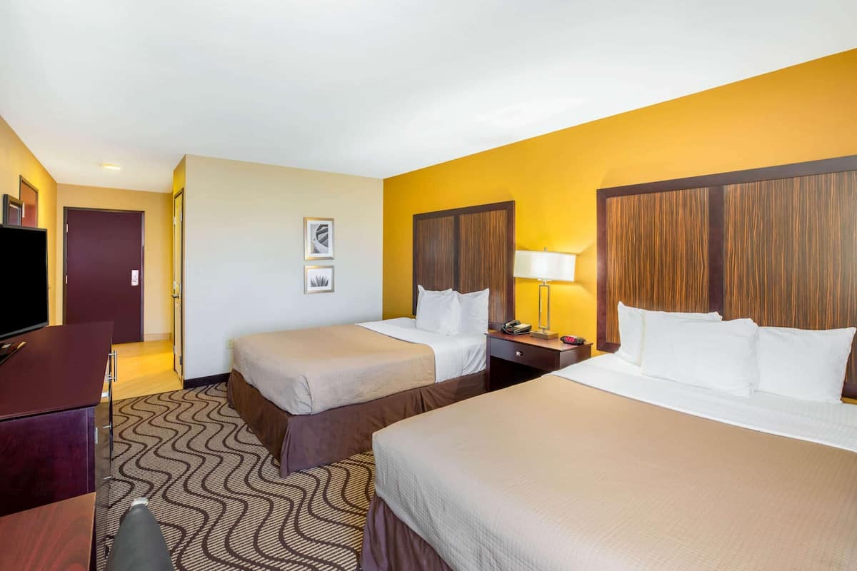 A hotel room with two beds, a desk, a TV, and a door.