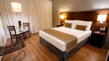 Una habitación de hotel con una cama grande, un escritorio, dos sillas y una lámpara.
