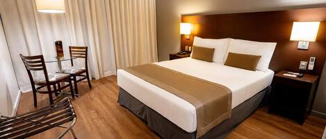 A hotel room with a large bed, a desk, two chairs, and a lamp.