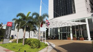 A modern hotel entrance with a glass facade, palm trees, and a clear blue sky. - Hotel Panamby São Paulo (São Paulo)