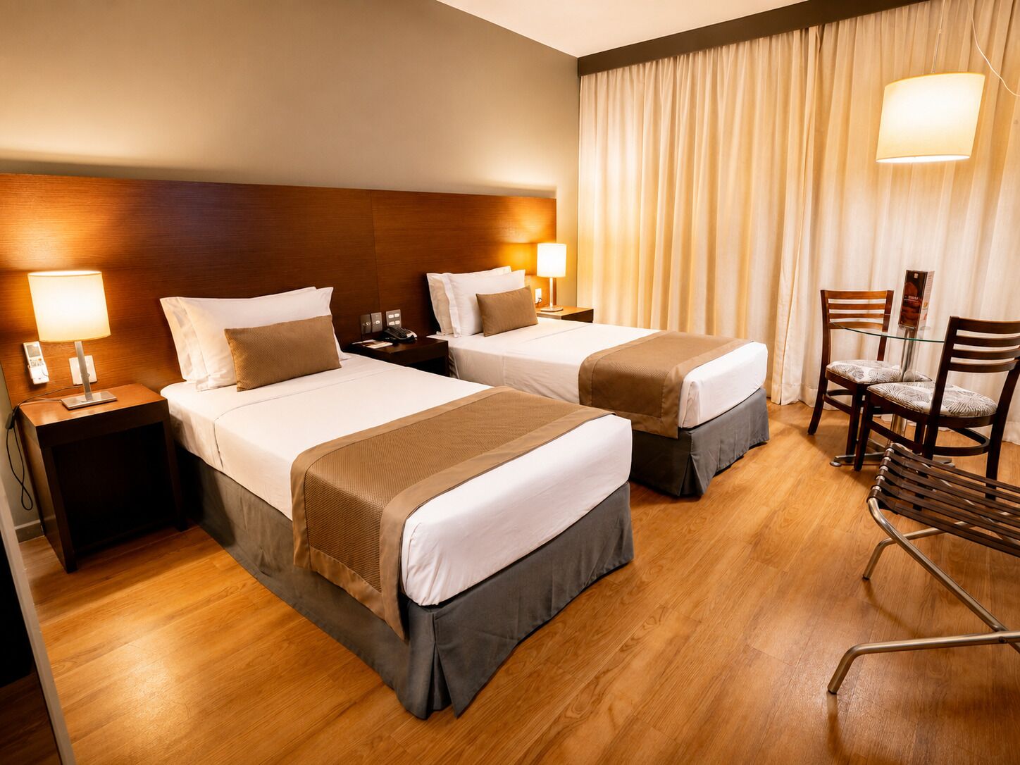 Ein Hotelzimmer mit zwei Betten, einem Schreibtisch, einem Sessel und einem Vorhang.