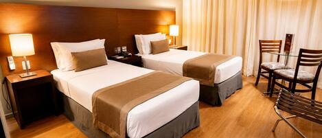 Ein Hotelzimmer mit zwei Betten, einem Schreibtisch, einem Sessel und einem Vorhang.