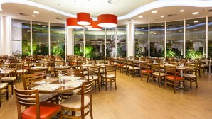 A spacious restaurant with multiple dining tables and chairs, large windows with greenery, and modern ceiling lights. - Hotel Panamby São Paulo (São Paulo)