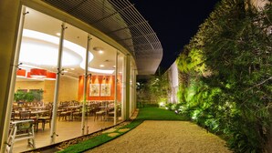 A modern building with a glass facade, a well-lit interior, and a pathway leading to a green area with trees. - Hotel Panamby São Paulo (São Paulo)