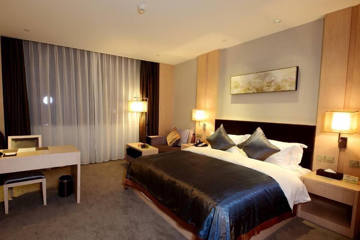 A hotel room with a large bed, bedside tables with lamps, a desk, and a chair.