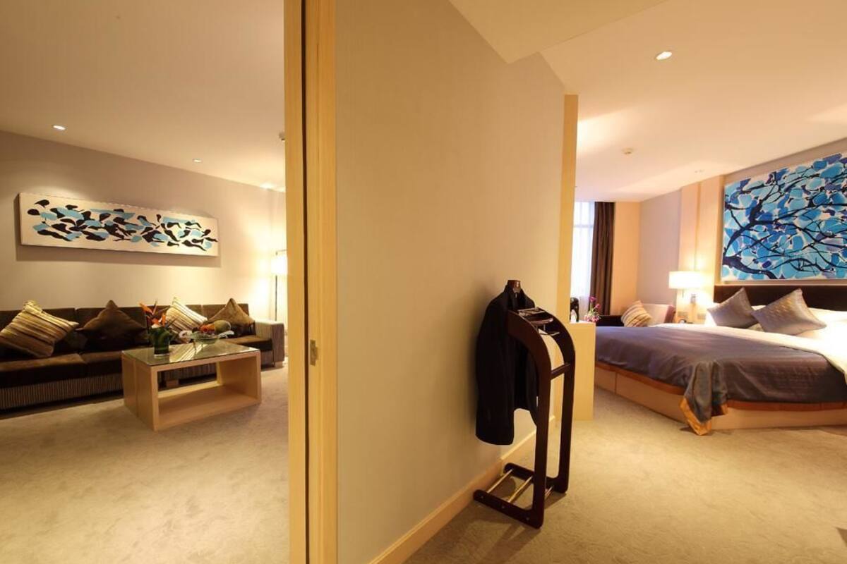 A modern hotel room with a sofa, a bed, a nightstand, and a wall art piece.