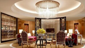 Un lobby lujoso con una gran araña, elegantes asientos y una pared decorativa con patrones geométricos.