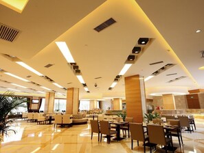 Eine großzügige Hotelhalle mit modernem Design, ausgestattet mit einer zentralen Sitzgruppe, mehreren Esstischen und einer gut beleuchteten Decke mit Einbaustrahlern.
