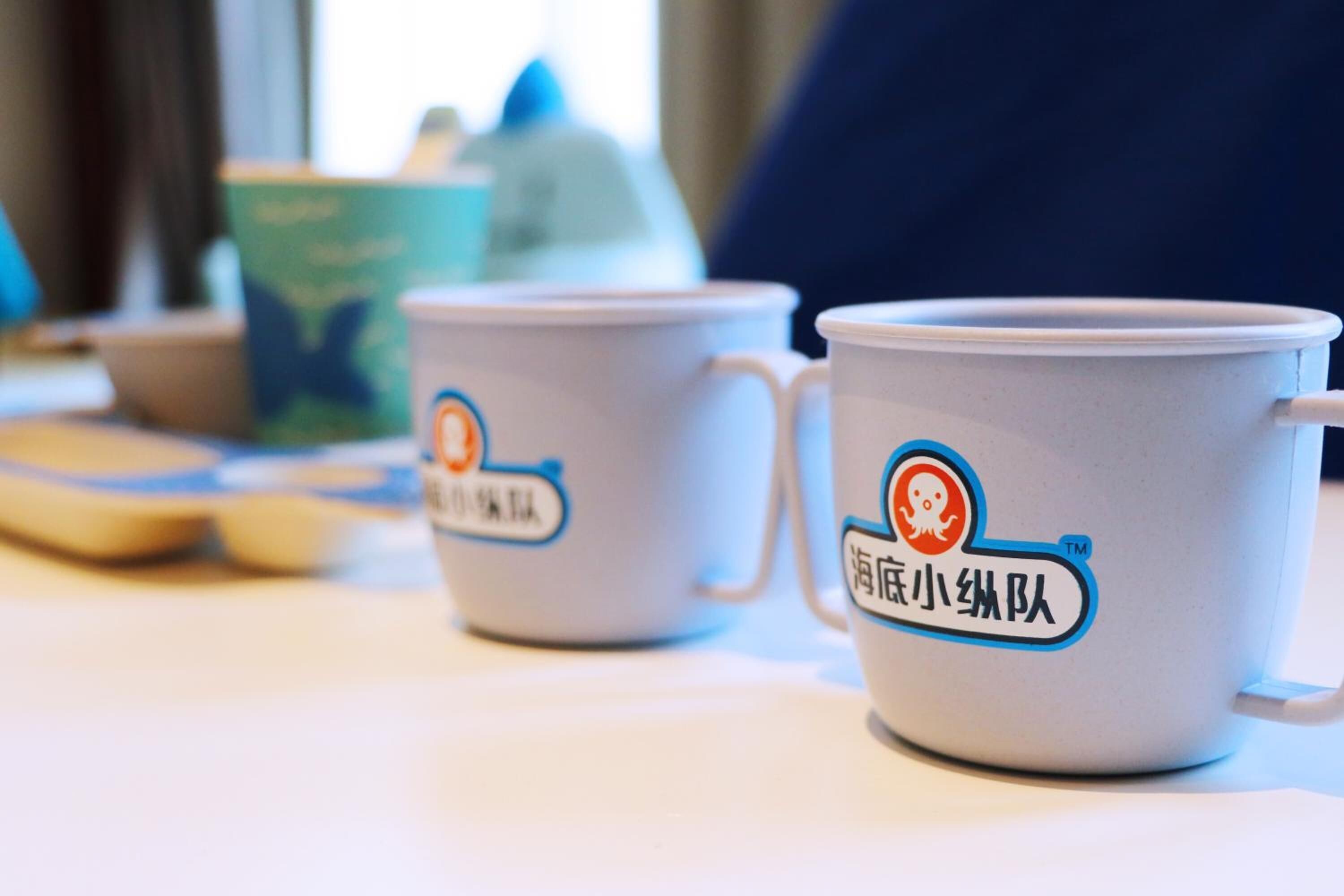 Two white mugs with blue and orange logos on a table.