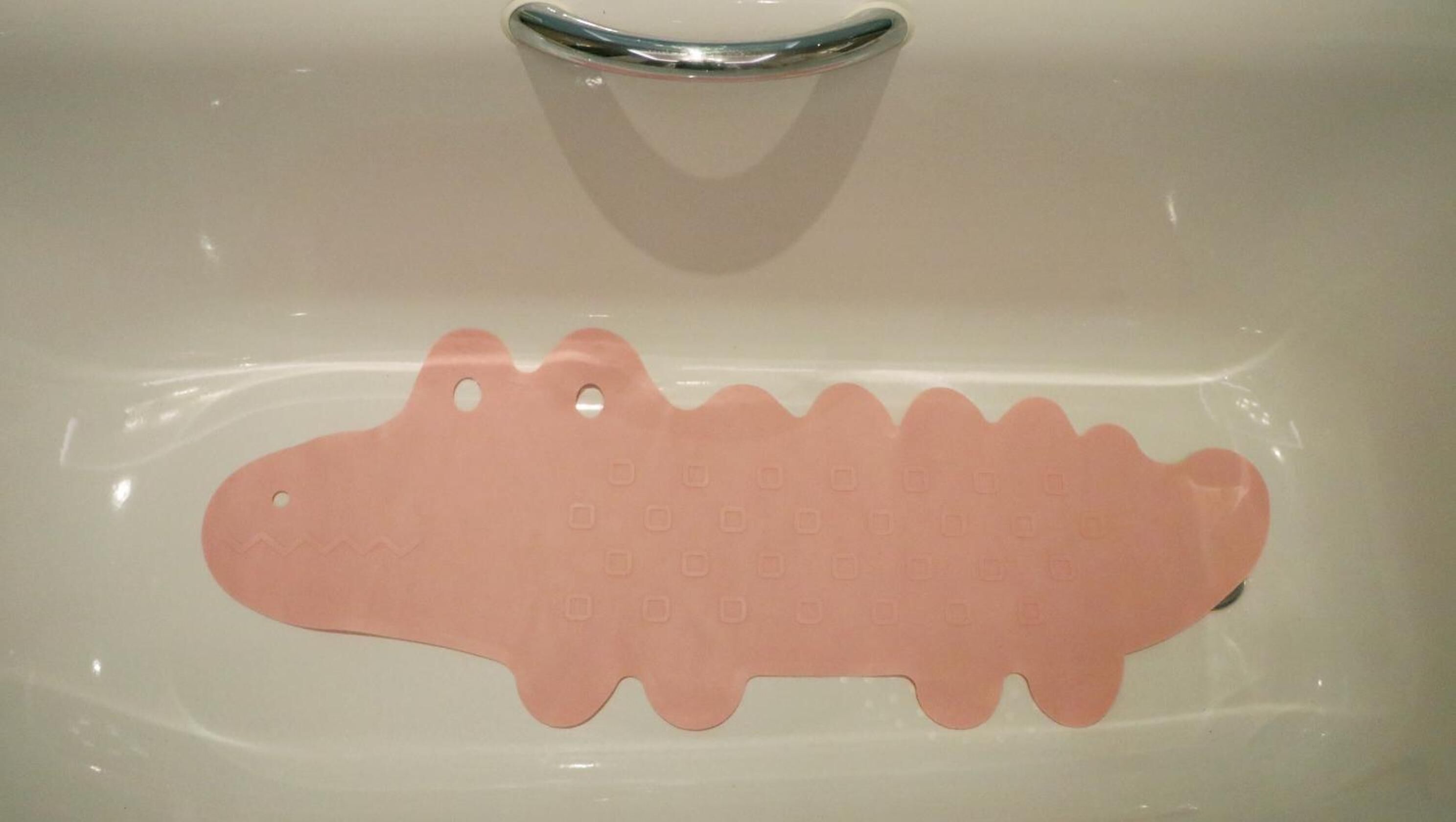 A bathtub with a pink bath mat shaped like a crocodile.