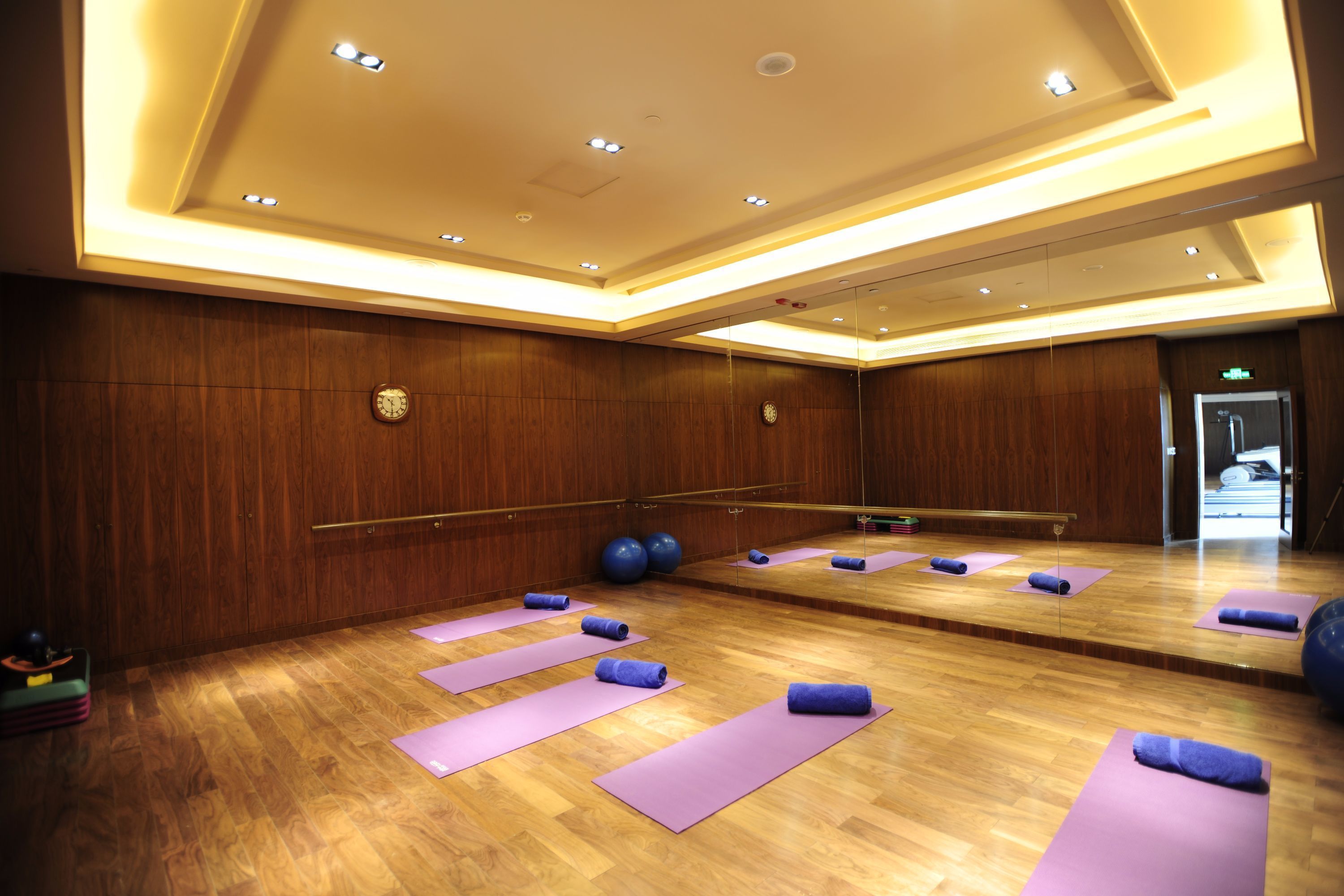 A spacious room with wooden floors, large mirrors, and purple yoga mats arranged for exercise.